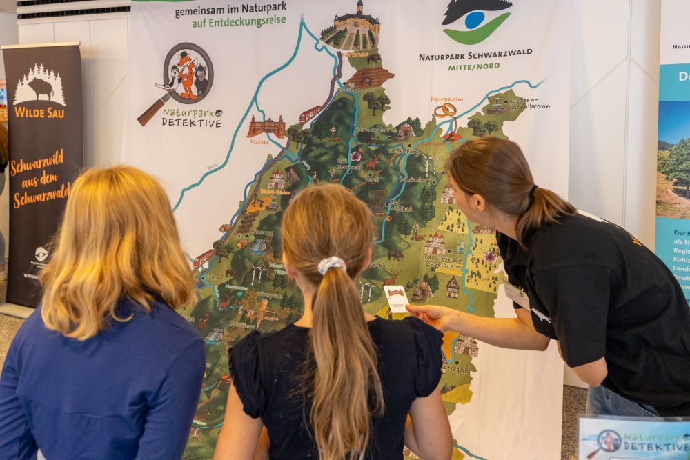 Eine Frau zeigt zwei Mädchen die Naturpark-Karte.