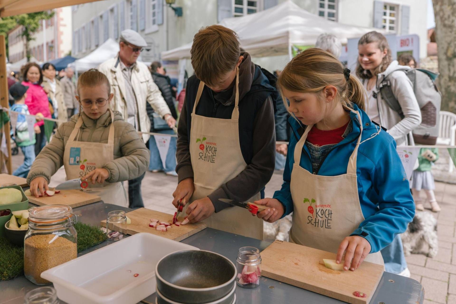 Drei Kinder schneiden an einem Stand Gemüse.