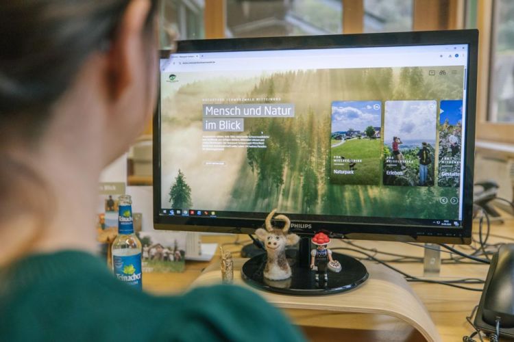 Eine Frau sitzt am Schreibtisch und schaut auf einen Bildschirm, der die neue Naturpark-Webseite zeigt.