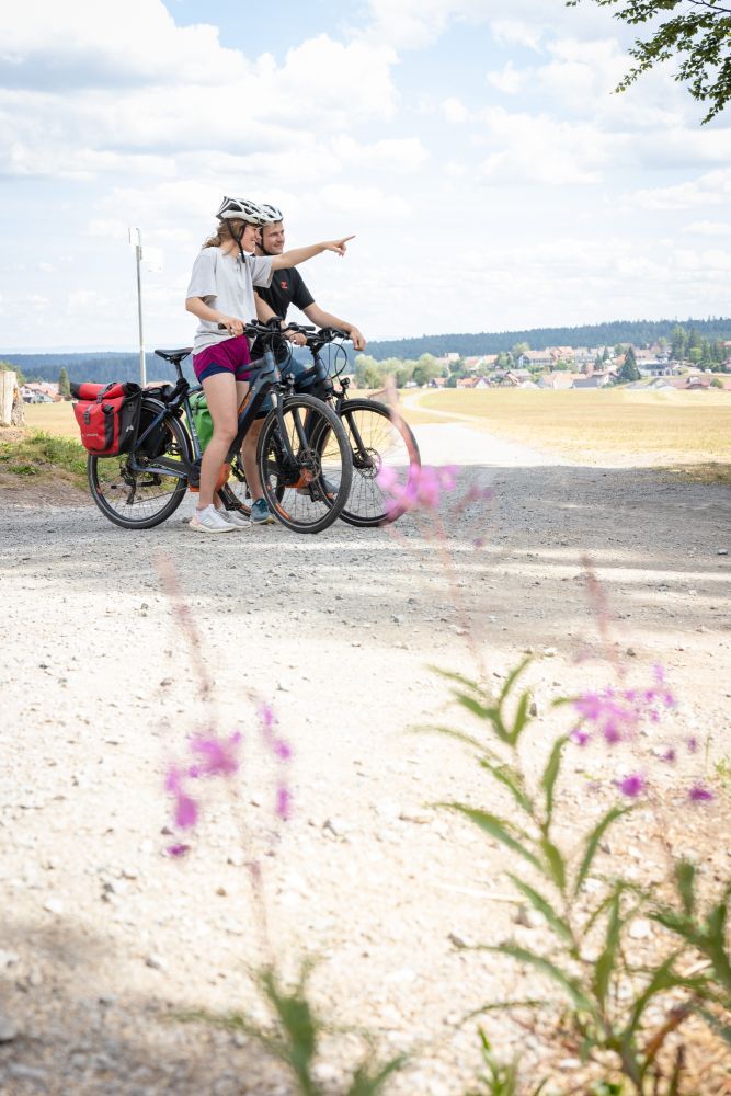 Eine Frau und ein Mann stehen mit ihren Fahrrädern auf einem Kiesweg und schauen in die Ferne.