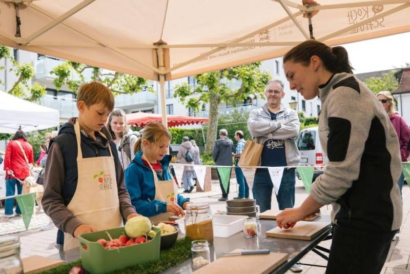 Eine Frau schneidet mit Kindern an einem Tisch Gemüse.
