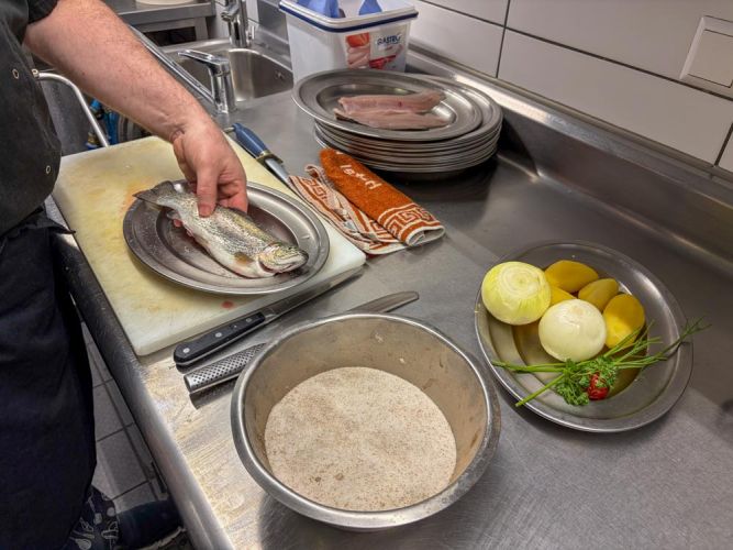 Zutaten für die Forelle: Gewürzmischung, Zwiebeln, Kartoffeln, Petersilie und Forelle auf Teller und in Schüsseln in der Küche angerichtet