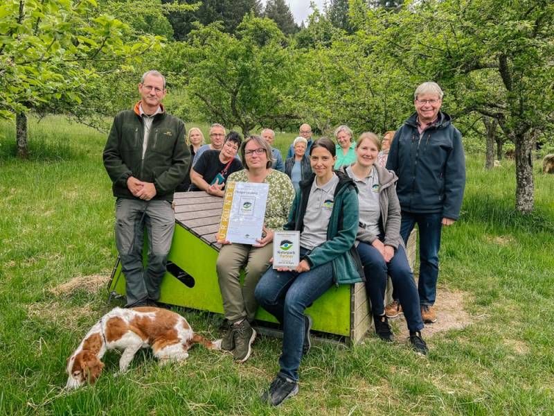 Menschen sitzen auf einer Holzliege inmitten einer Streuobstwiese
