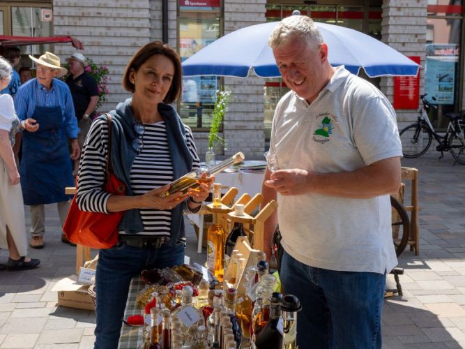 Frau hält Likörflasche an einem Markt-Stand in der Hand.