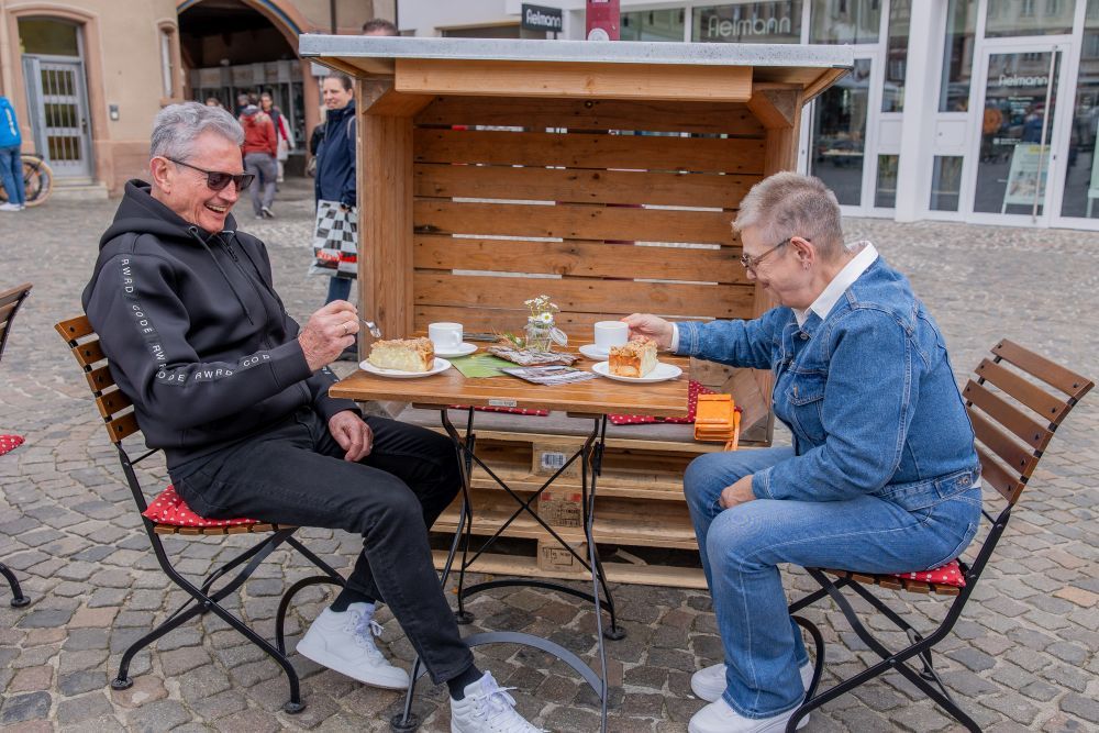 Ein Mann und eine Frau sitzen bei Kaffe und Kuchen an einem kleinen Gartentisch.