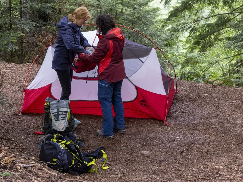 Zwei Frauen bauen im Wald ein Zelt ab.