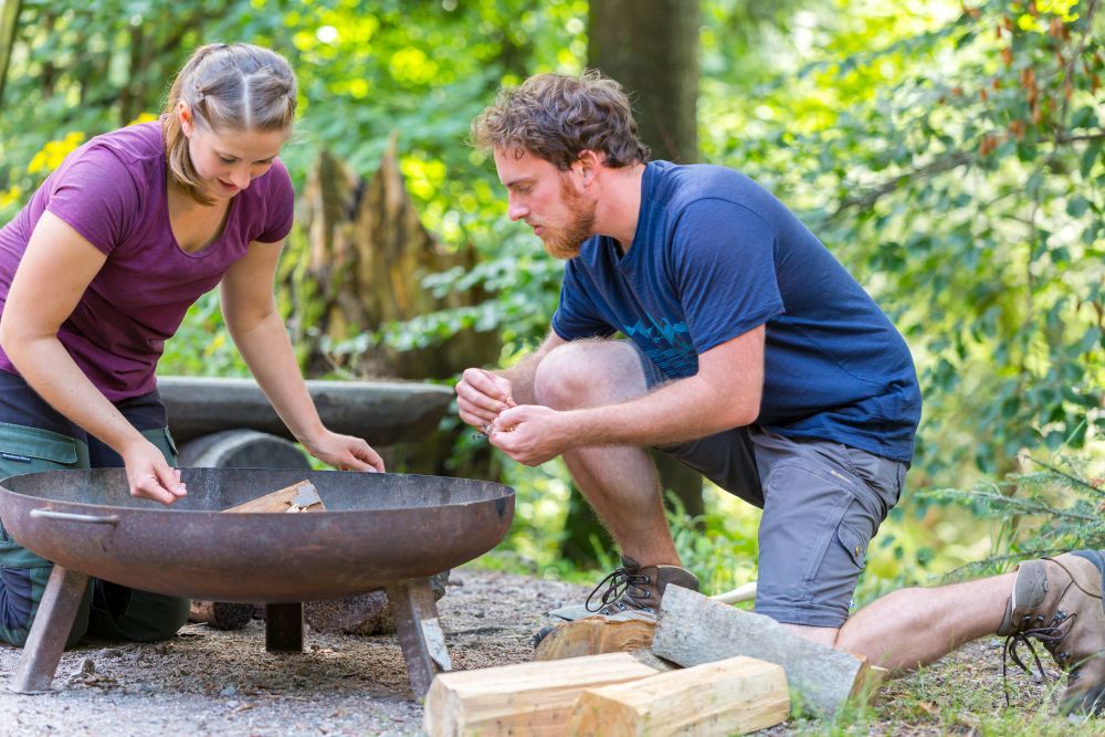 Ein Mann und eine Frau machen Feuer in einer Feuerschale.