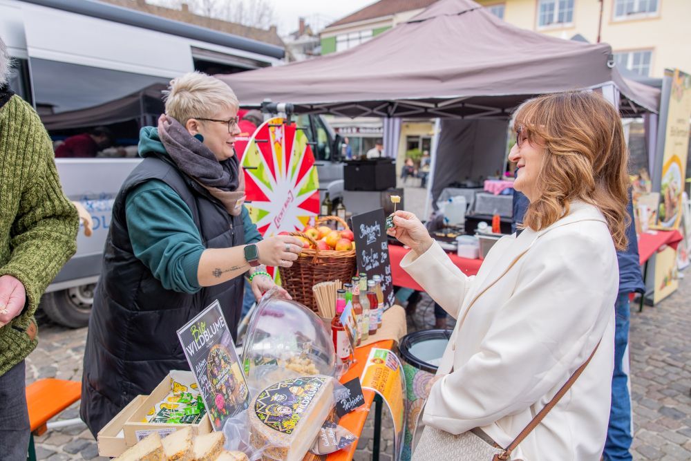 Eine Frau probiert Käse an einem Markt-Stand.