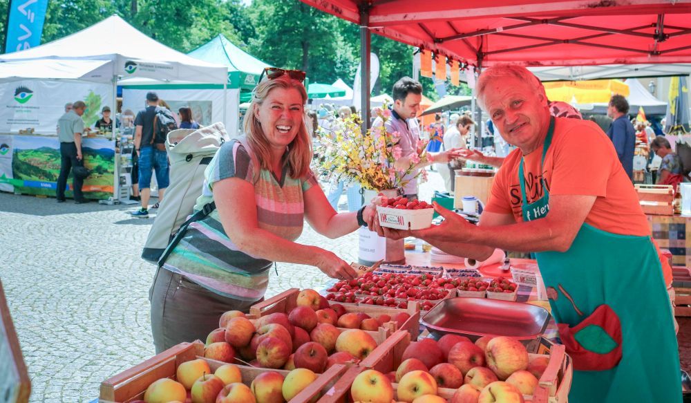Eine Frau kauft am Obst-Stand eines Mannes Erdbeeren.