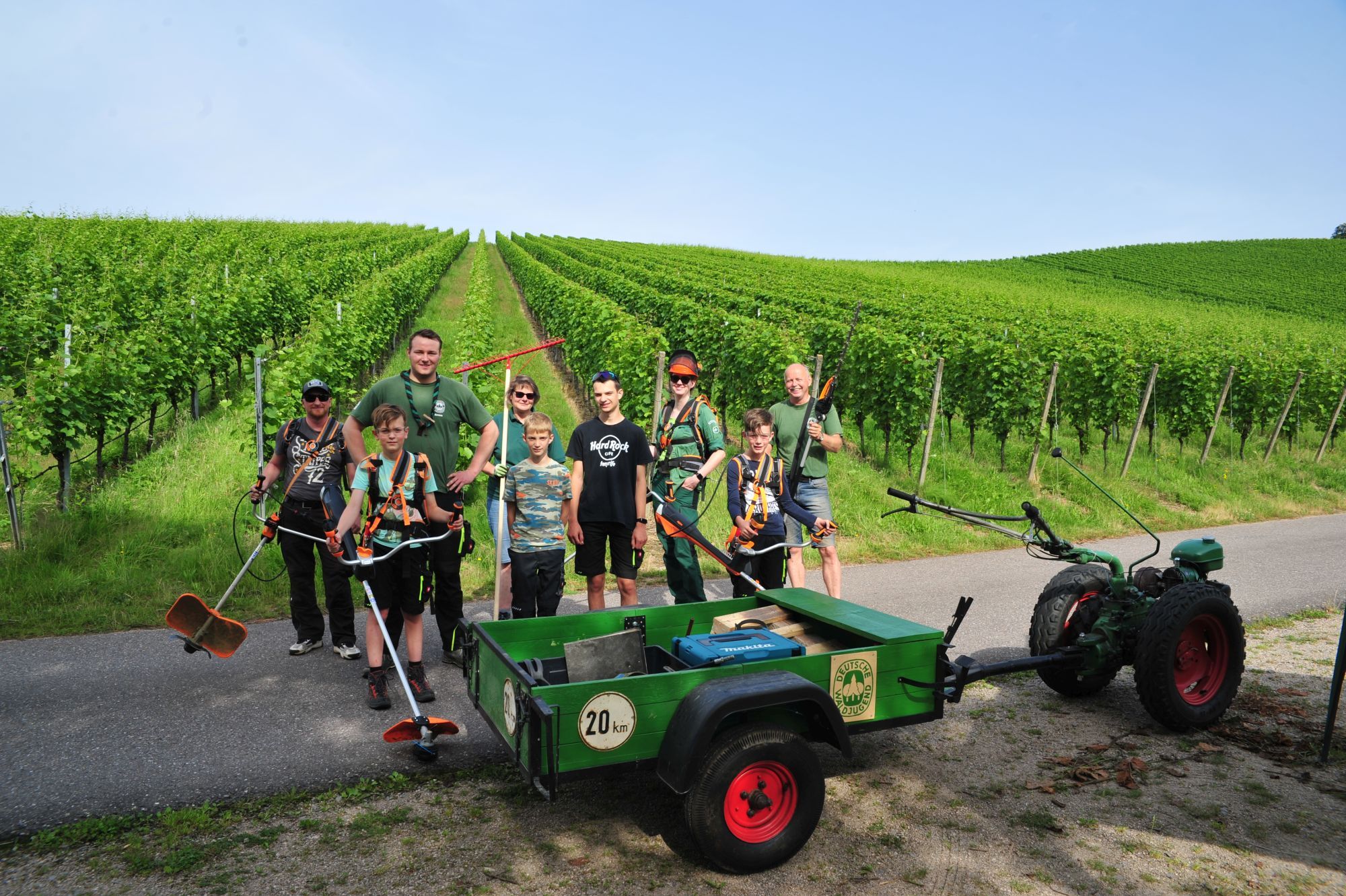 Helfende stehen mit Maschinen für die Landschaftspflege vor Weinreben.