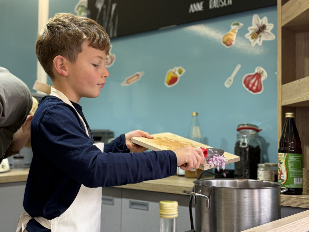 Junge gibt gehackte Zwiebeln in einen Topf