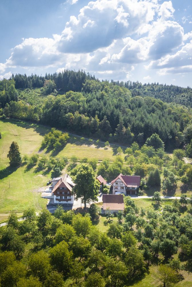 Ein Hof im Fachwerkstil liegt umgeben von Streuobstwiesen und Wald