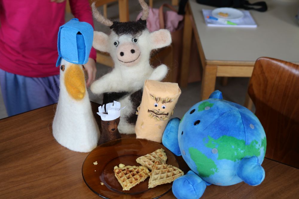 Die Figuren des Klima-Kochtheaters sitzen vor einem Teller mit Waffeln.