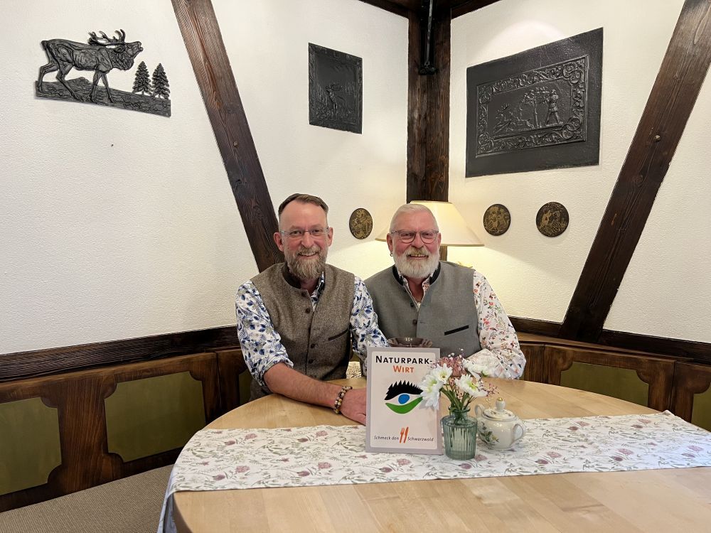 Arno Peiffer (l.) und Ralf Bischoff (r.) präsentieren an ihrem Lieblingsplatz in ihrem Landcafé Baiermühle in Altensteig die Auszeichnung als „Naturpark-Wirt“ – ein Prädikat für regionale Küche.