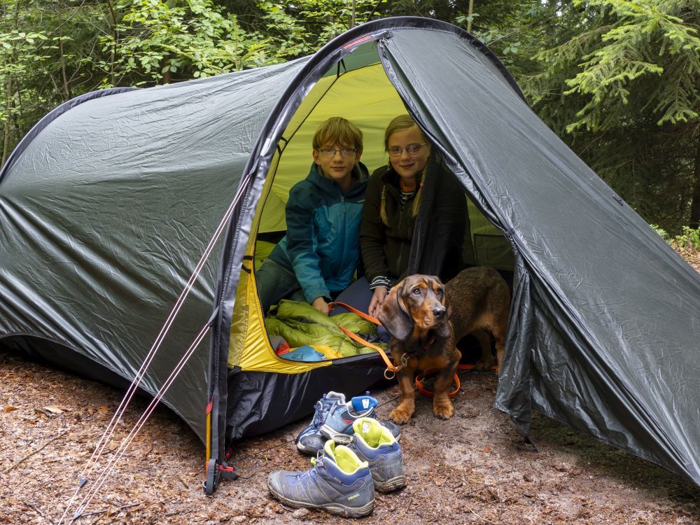 Ein Junge und ein Mädchen sitzen mit Hund in einem Zelt.
